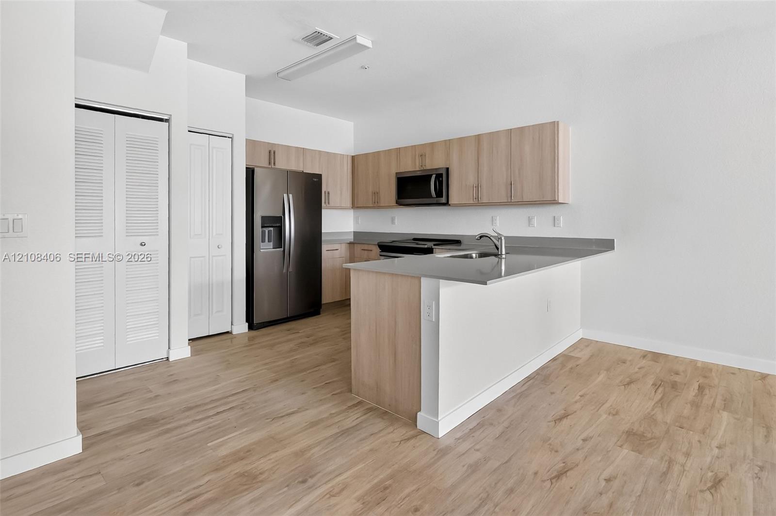 Kitchen featuring light wood-finish cabinetry, solid surface countertops, stainless steel appliances, and wood-finish flooring