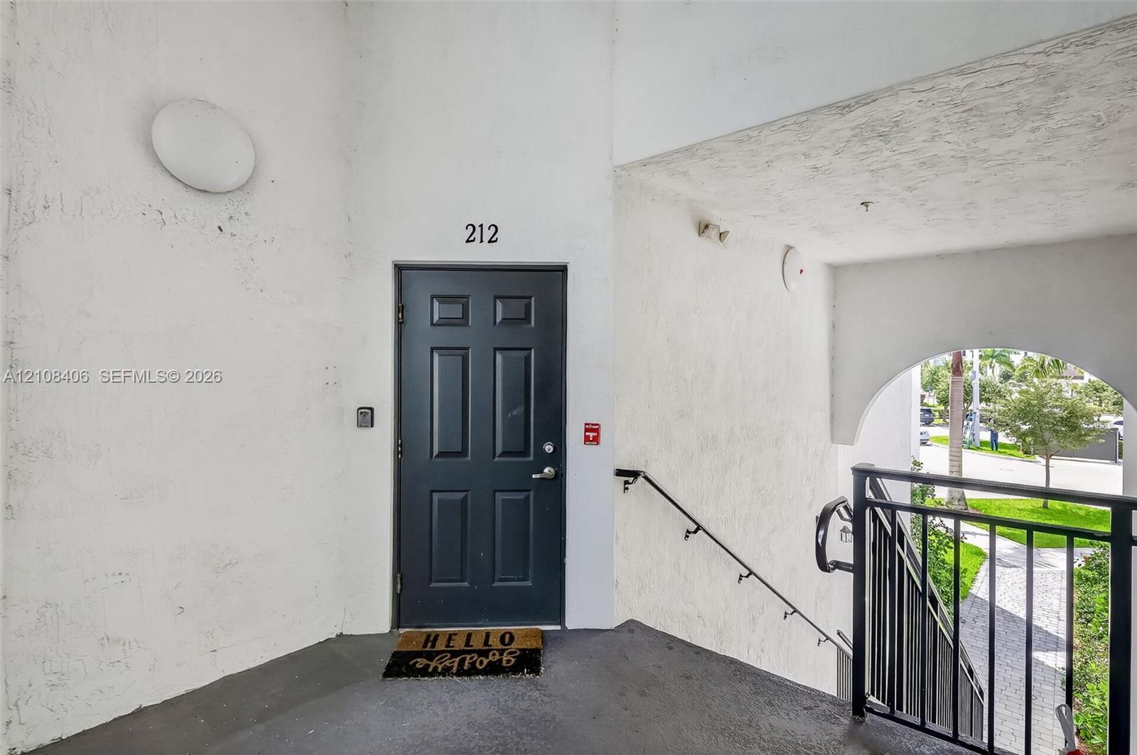 Exterior entry featuring a dark-toned paneled door, textured wall finish, and an arched entryway with a black metal railing
