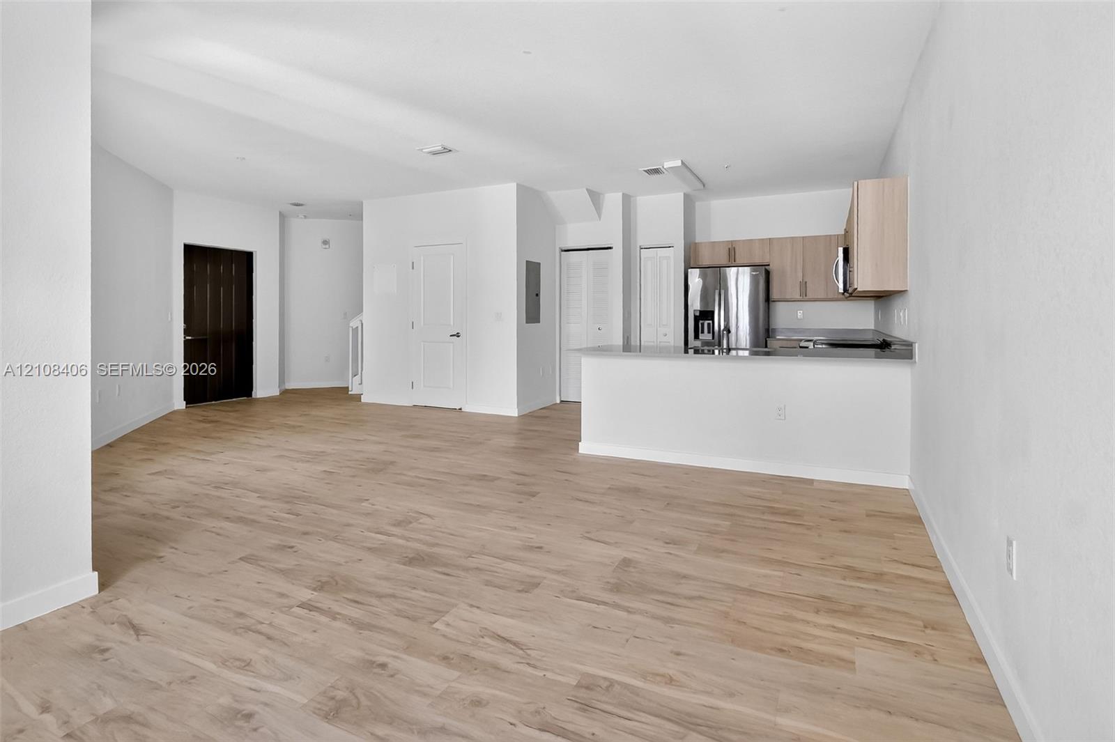 Open floor plan featuring wood-finish flooring, kitchen with light-tone cabinetry, stainless steel refrigerator, and a breakfast bar