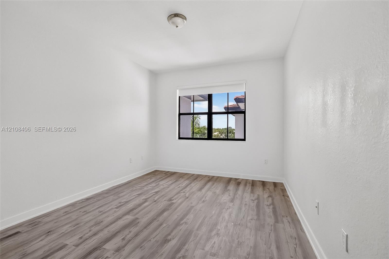 Interior space featuring wood-finish flooring, white walls, and a multi-pane window with black framing