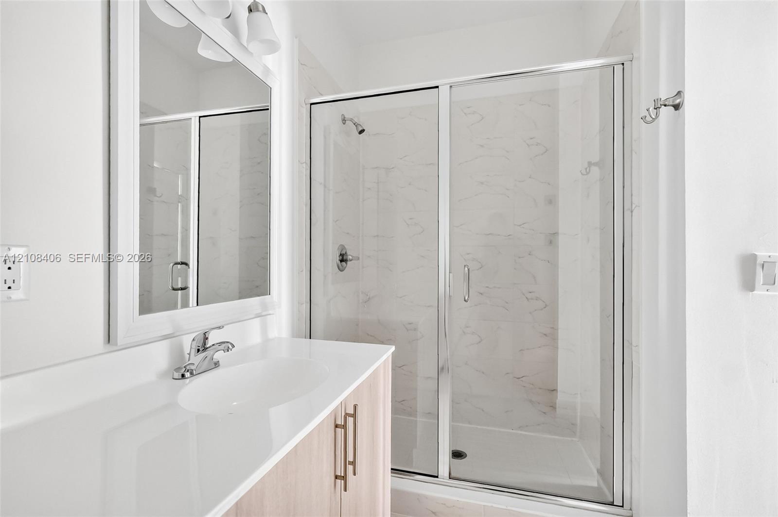 Bathroom featuring a light wood-finish vanity with a white countertop, walk-in shower with a glass enclosure, and wall-mounted mirror with integrated light fixtures