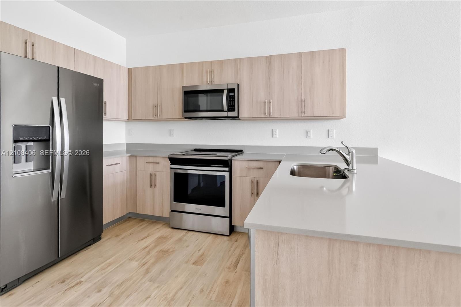 Kitchen featuring light-finish cabinetry, stainless steel appliances, quartz countertops, a dual-basin stainless steel sink, and wood-finish flooring