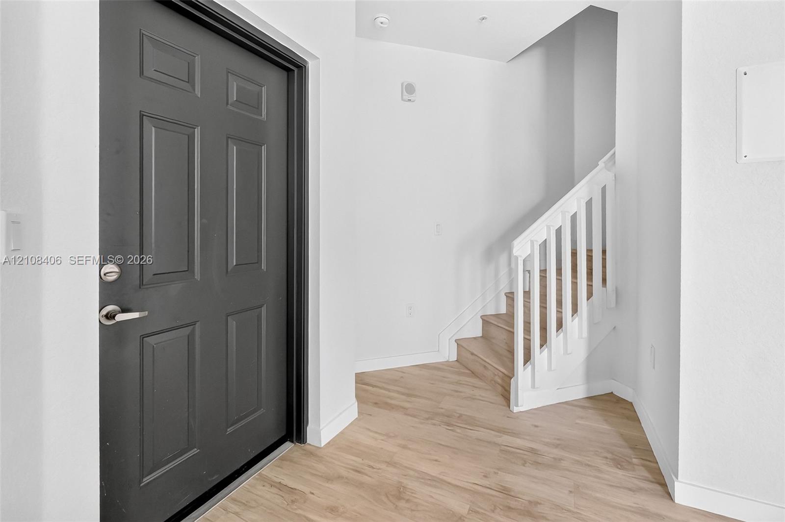 Entryway featuring a dark-finish paneled door, wood-finish flooring, and a staircase with white balusters and wood-finish treads