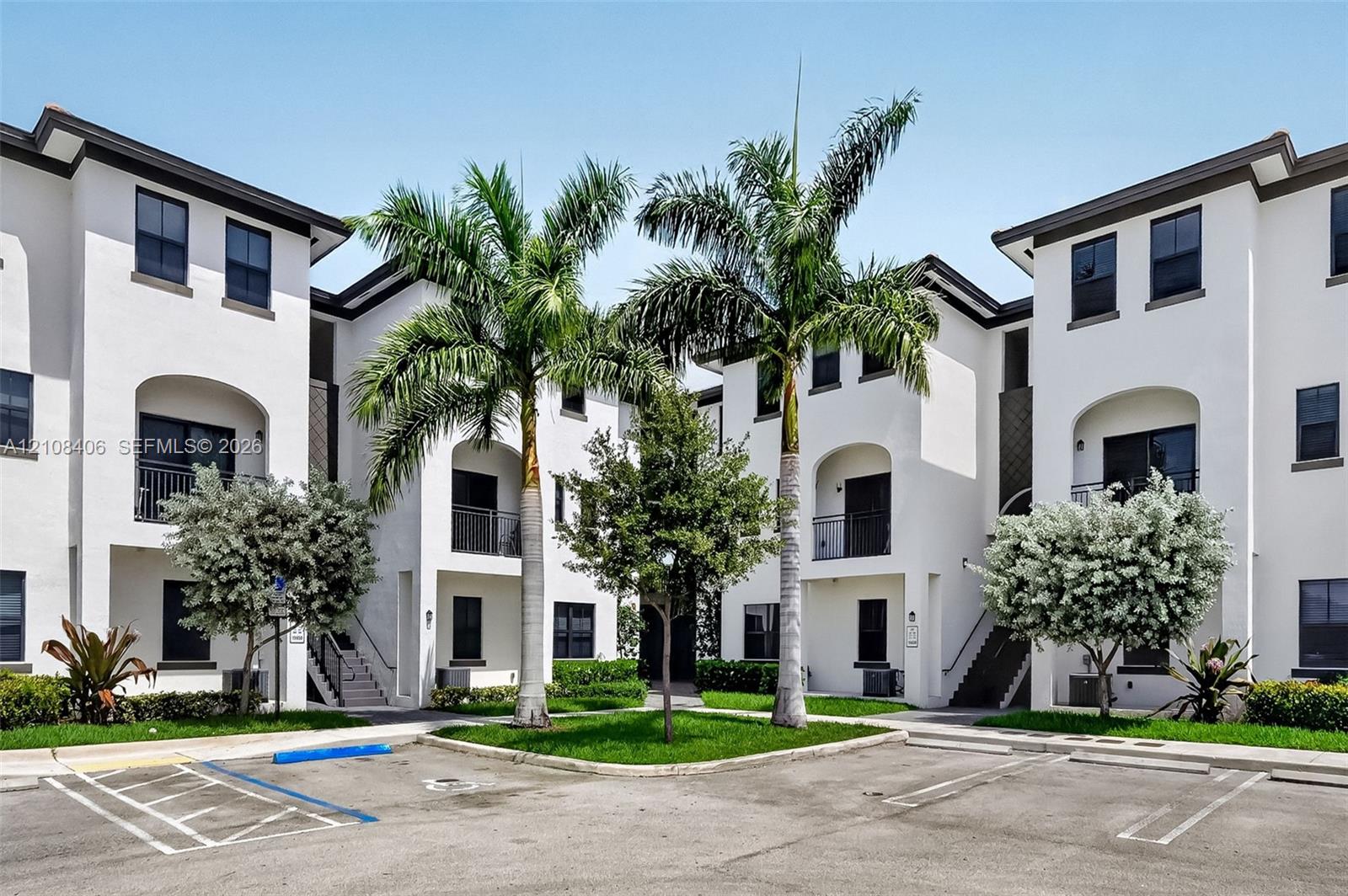 Stucco exterior featuring arched entryways, balconies with metal railings, and multi-level design, complemented by a landscaped courtyard with palm trees and manicured lawns