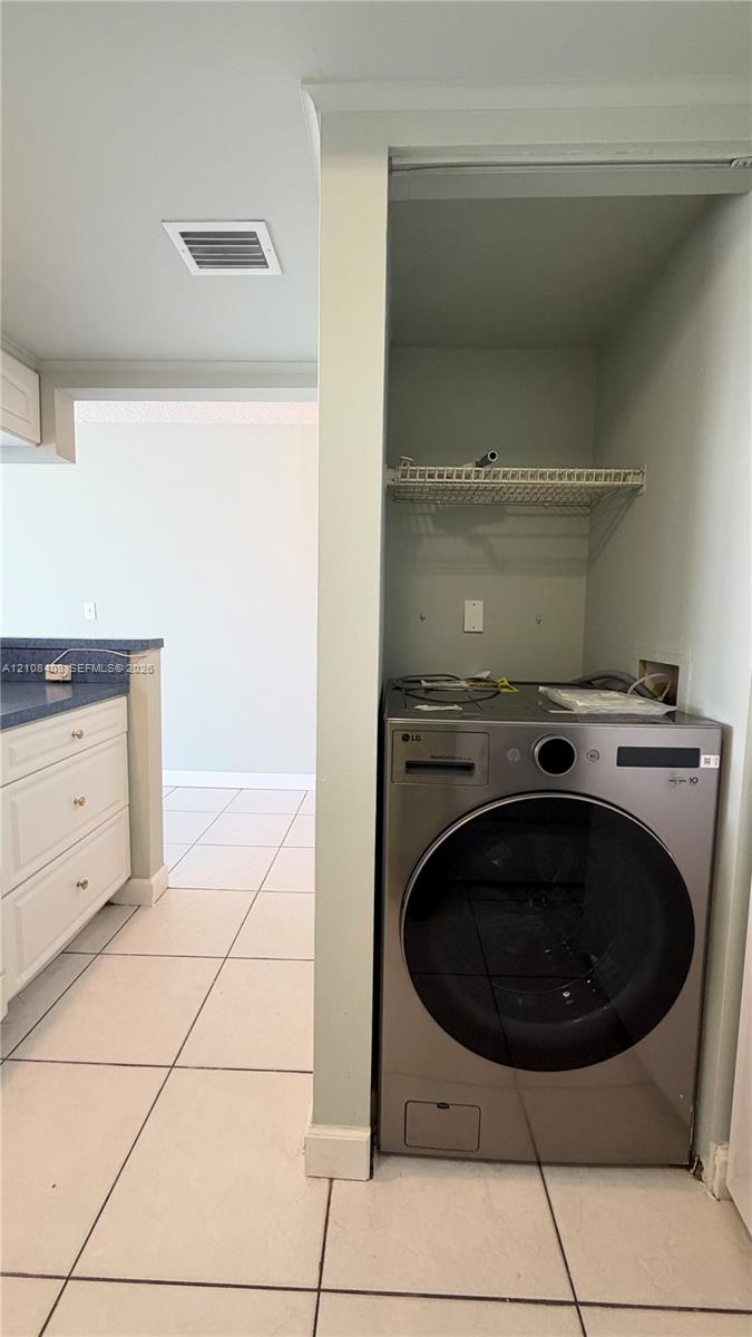 Laundry alcove featuring a stainless steel front-load washer, wire shelving, and neutral floor tile Laundry alcove featuring a stainless steel front-load washer, wire shelving, and neutral floor tile