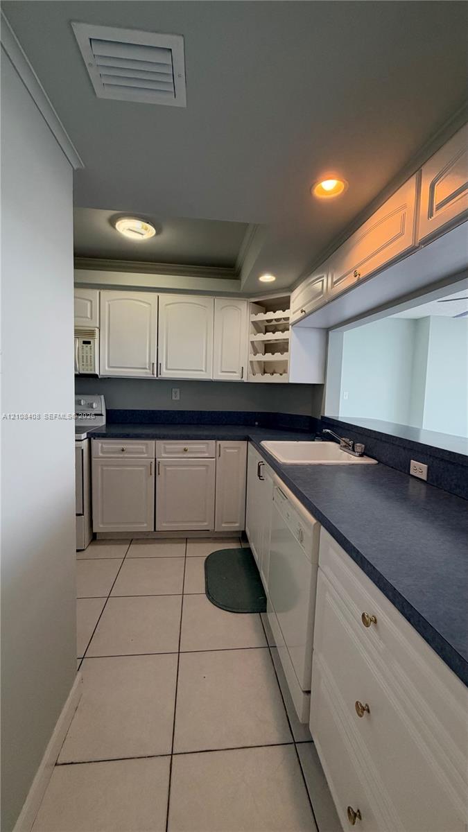 Kitchen featuring white cabinetry with integrated wine rack, solid-surface countertops, white porcelain sink, tile flooring, and recessed lighting Kitchen featuring white cabinetry with integrated wine rack, solid-surface countertops, white porcelain sink, tile flooring, and recessed lighting