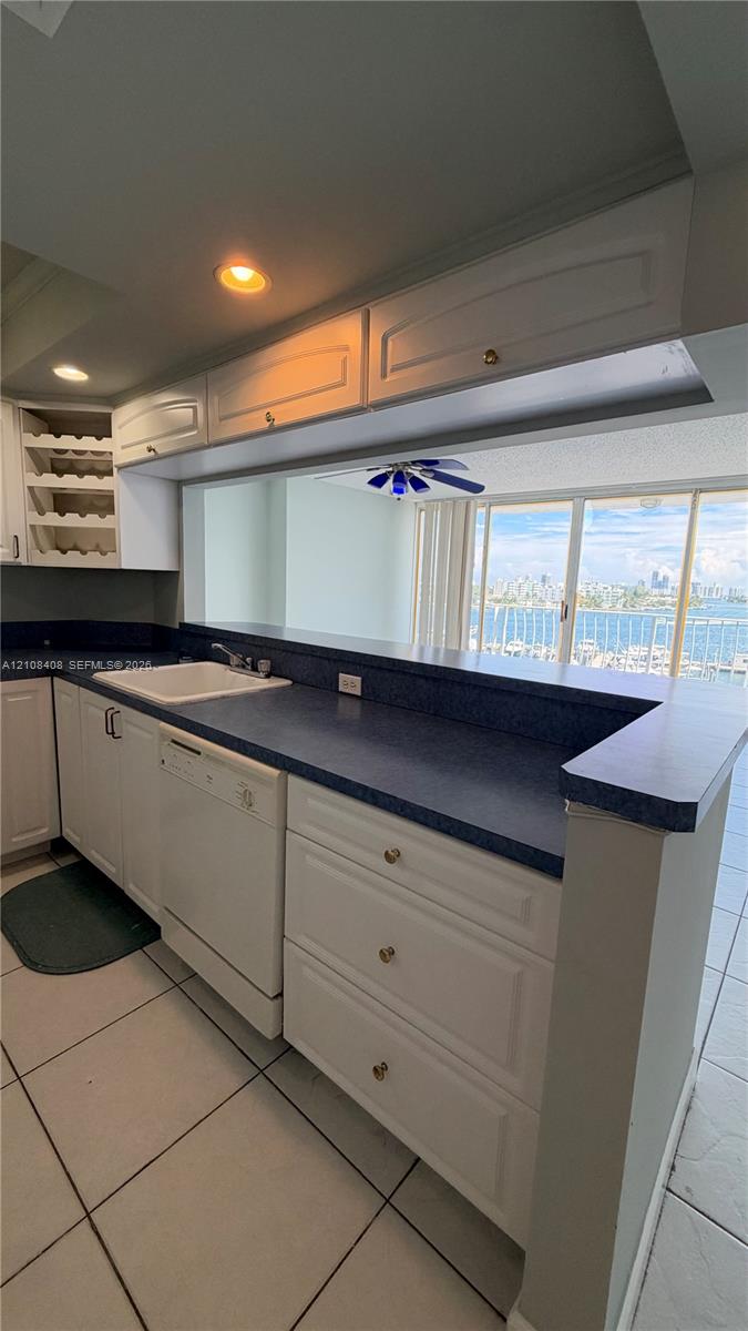 Kitchen featuring white cabinetry with integrated wine storage, contrasting countertops, built-in dishwasher, recessed lighting, and tile flooring Kitchen featuring white cabinetry with integrated wine storage, contrasting countertops, built-in dishwasher, recessed lighting, and tile flooring