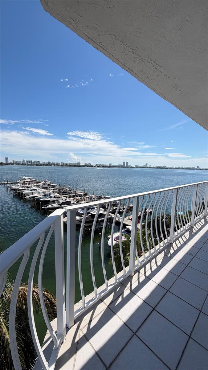 Covered balcony featuring white tile flooring and a decorative white metal railing, overlooking a marina and open water Covered balcony featuring white tile flooring and a decorative white metal railing, overlooking a marina and open water