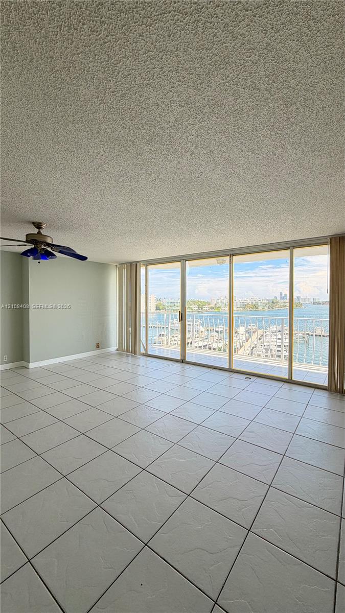 Living area featuring floor-to-ceiling sliding glass doors, ceramic tile flooring, a ceiling fan, and balcony access with water and marina scenery