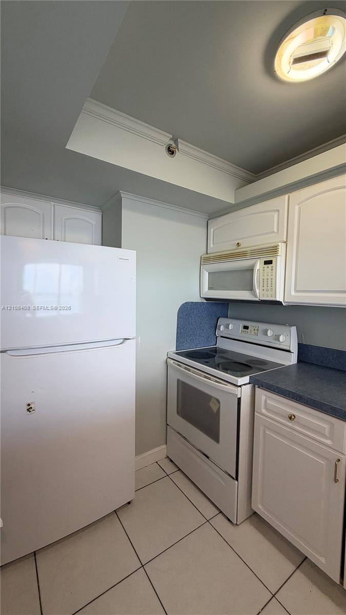 Kitchen featuring white cabinetry, solid-surface countertops, tile flooring, and built-in appliances including a refrigerator, electric range, and over-the-range microwave Kitchen featuring white cabinetry, solid-surface countertops, tile flooring, and built-in appliances including a refrigerator, electric range, and over-the-range microwave