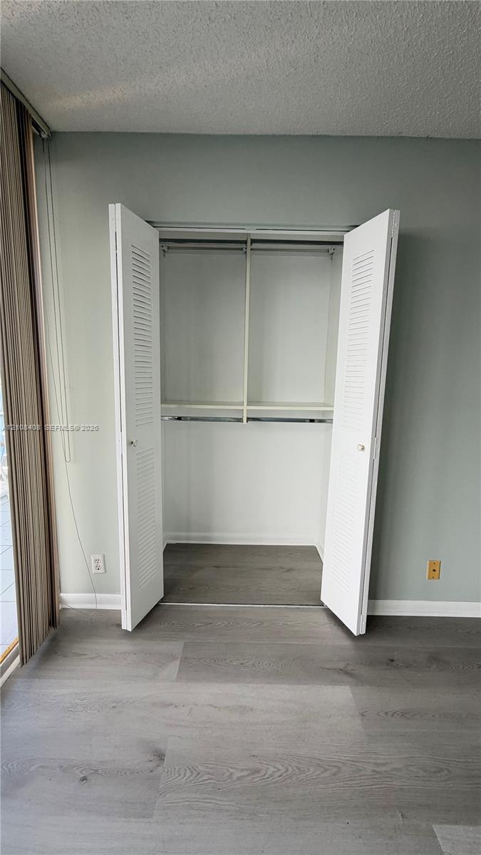 Closet featuring white louvered bifold doors, integrated shelving, and metal hanging rods, complemented by wood-finish flooring