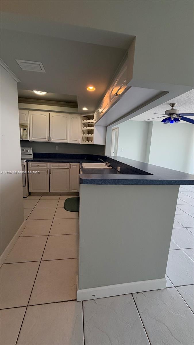 Kitchen featuring white cabinetry, solid-surface countertops, a breakfast bar, built-in wine rack, and tile flooring Kitchen featuring white cabinetry, solid-surface countertops, a breakfast bar, built-in wine rack, and tile flooring