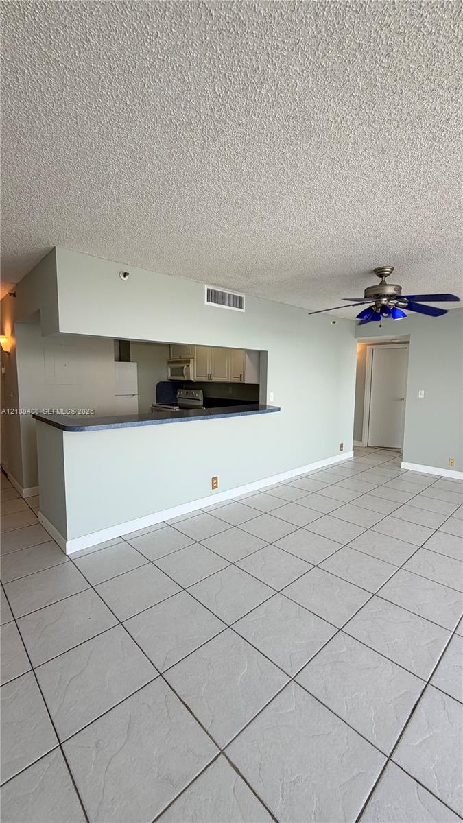 Open-concept interior featuring large-format tile flooring, a breakfast bar with dark surfacing, a ceiling fan, and built-in cabinetry Open-concept interior featuring large-format tile flooring, a breakfast bar with dark surfacing, a ceiling fan, and built-in cabinetry