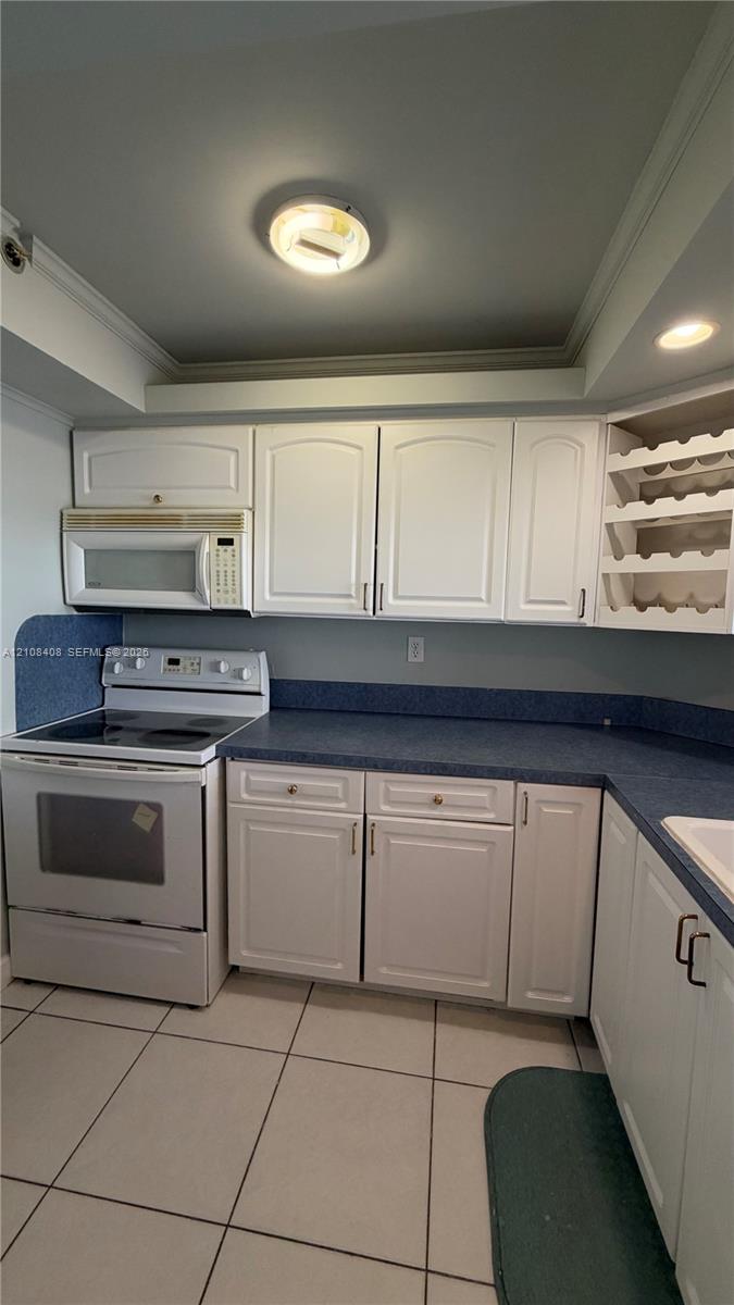 Kitchen featuring white shaker-style cabinetry, a built-in wine rack, solid-surface countertops with an integrated backsplash, and tile flooring Kitchen featuring white shaker-style cabinetry, a built-in wine rack, solid-surface countertops with an integrated backsplash, and tile flooring