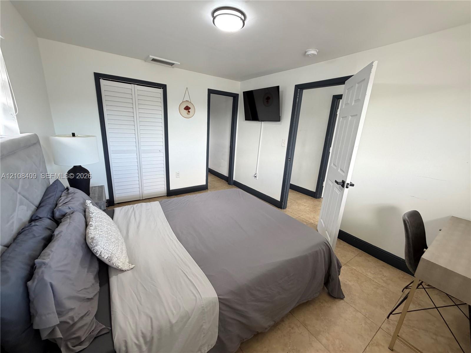 Bedroom featuring tile flooring, louvered closet doors, and contrasting dark-toned door trim