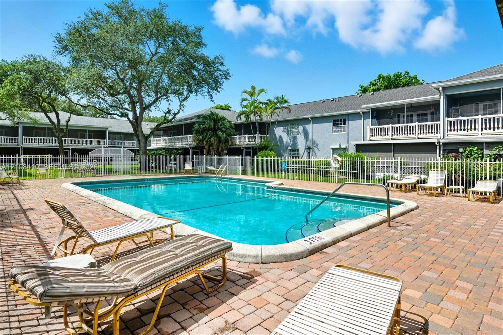 In-ground swimming pool featuring a brick paver surround and perimeter security fencing