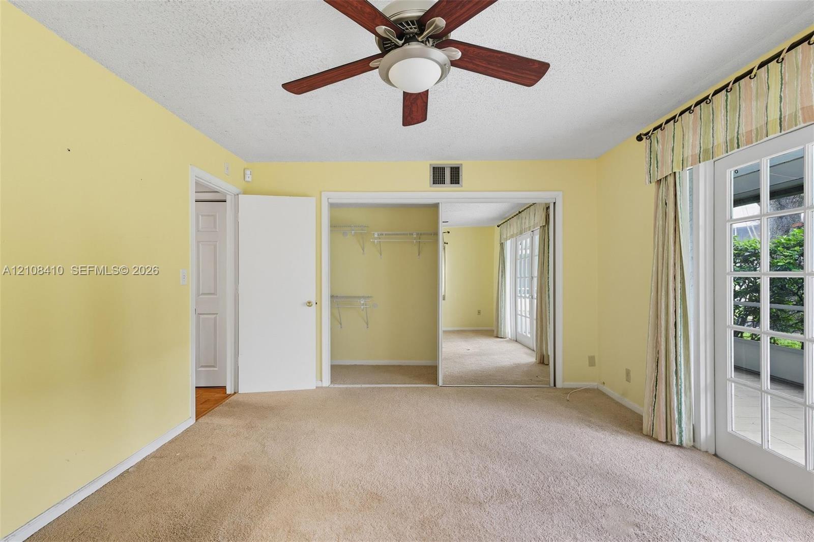 Ceiling fan with central lighting, dual-sliding mirrored closet doors with integrated shelving, and a glass-paneled exterior door