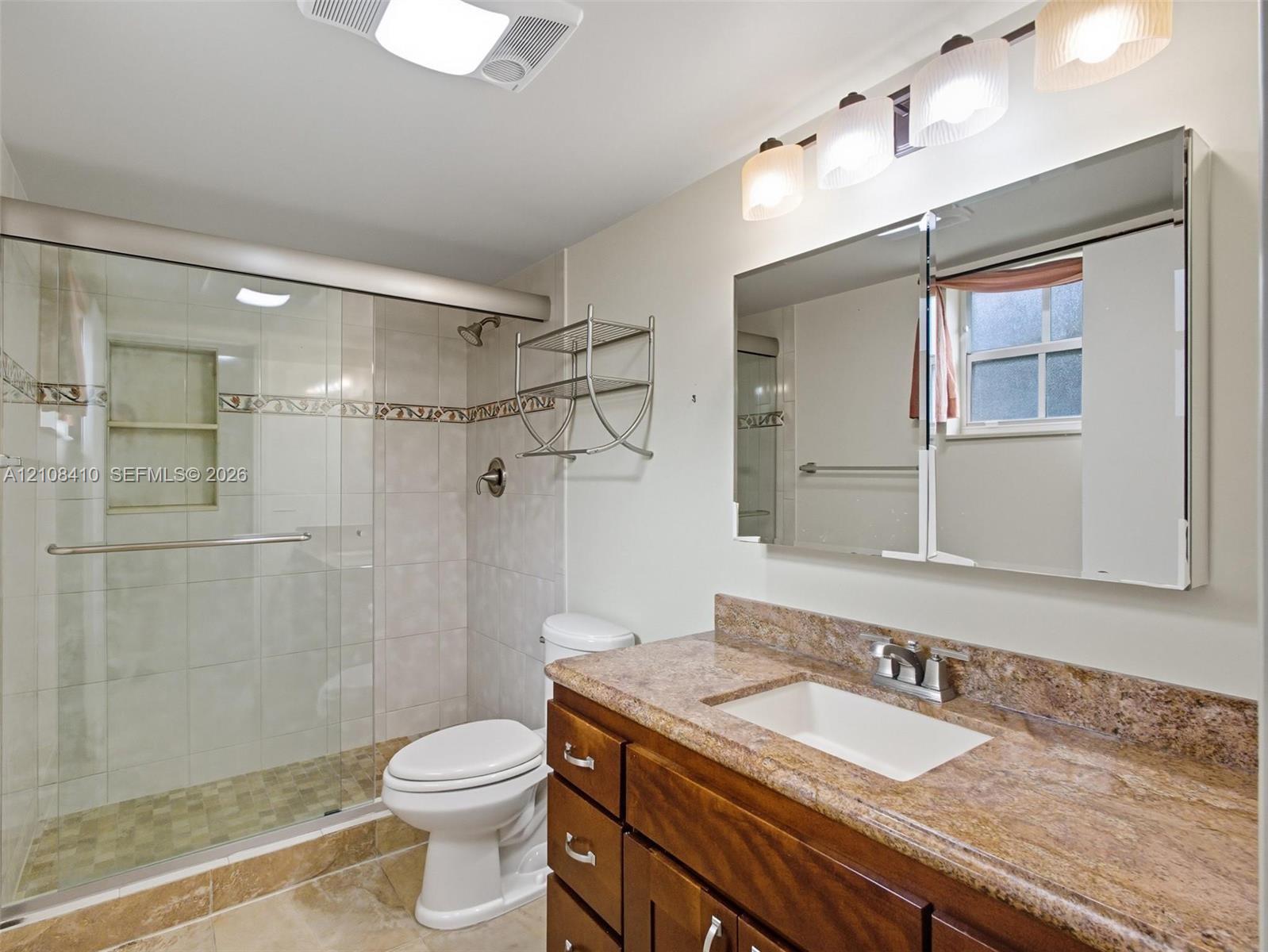 Bathroom featuring a vanity with a stone countertop, an integrated rectangular sink, a glass-enclosed shower with tiled walls and decorative inlay, and a built-in mirrored medicine cabinet