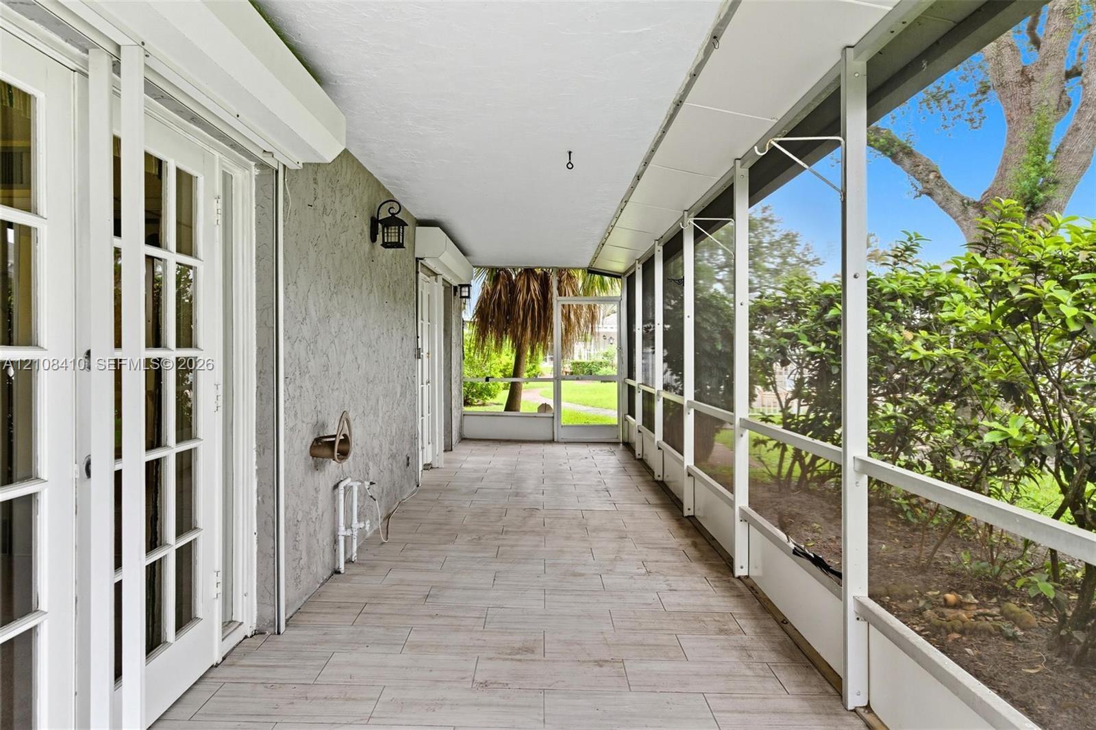 Screened-in porch featuring tile flooring, metal framing, multiple glass-paned double doors, and exterior wall-mounted lighting