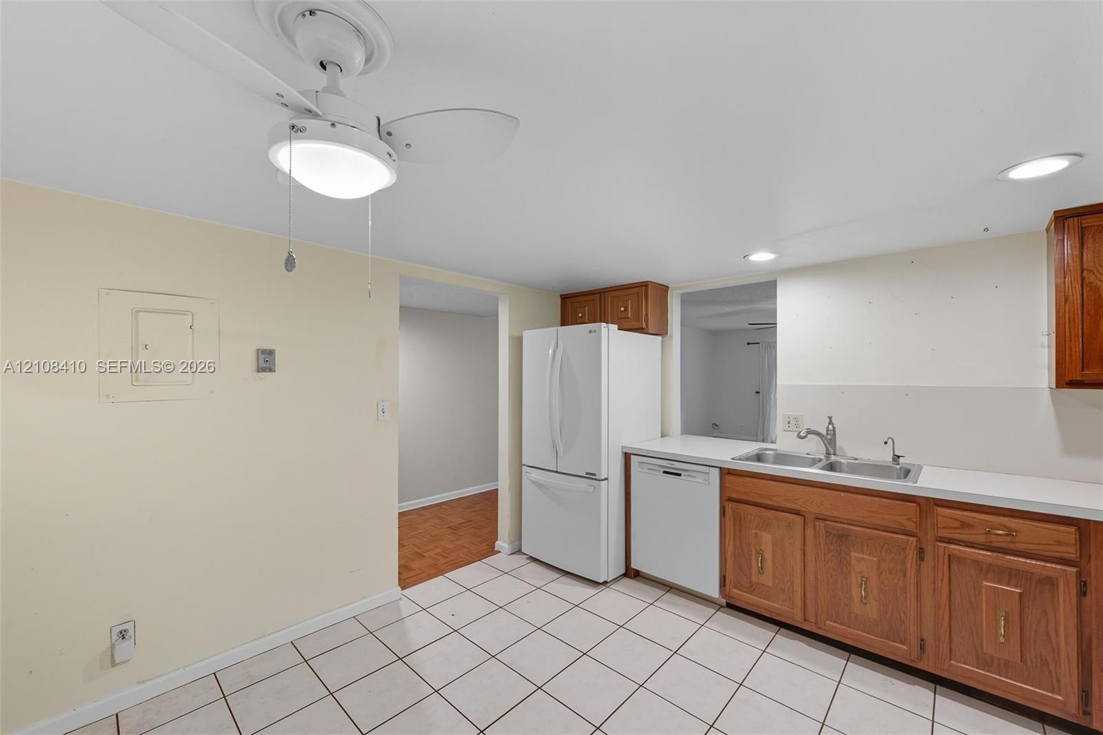 Kitchen featuring wood cabinetry, white appliances, a double-basin stainless steel sink, tiled flooring, and a ceiling-mounted light fixture Kitchen featuring wood cabinetry, white appliances, a double-basin stainless steel sink, tiled flooring, and a ceiling-mounted light fixture