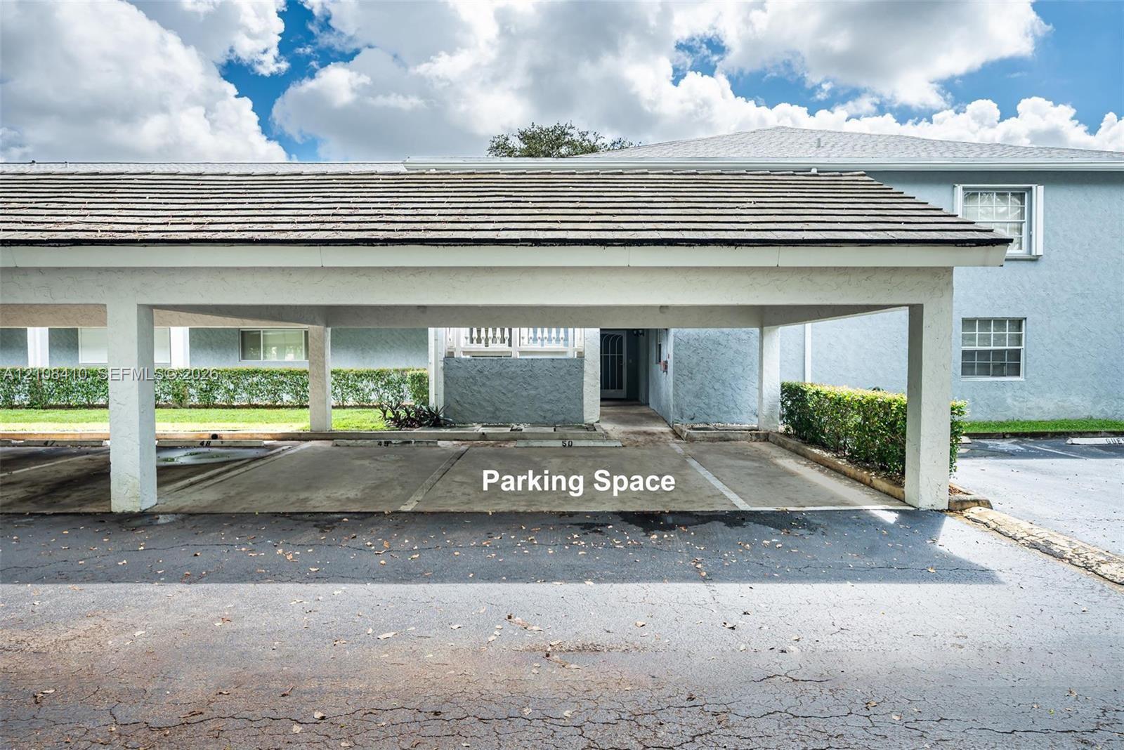 Covered parking structure featuring a shingled roof, concrete flooring, and support pillars, situated at the building exterior Covered parking structure featuring a shingled roof, concrete flooring, and support pillars, situated at the building exterior