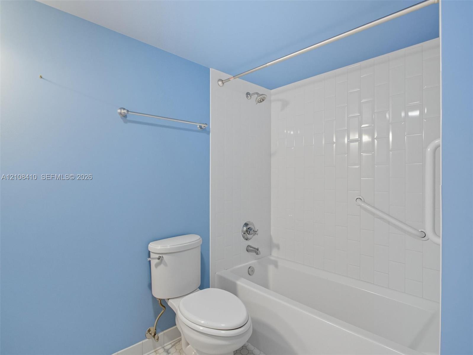 Bathroom featuring a porcelain tub and shower combination with vertical subway tile surround, polished chrome fixtures, and a dual-purpose grab bar