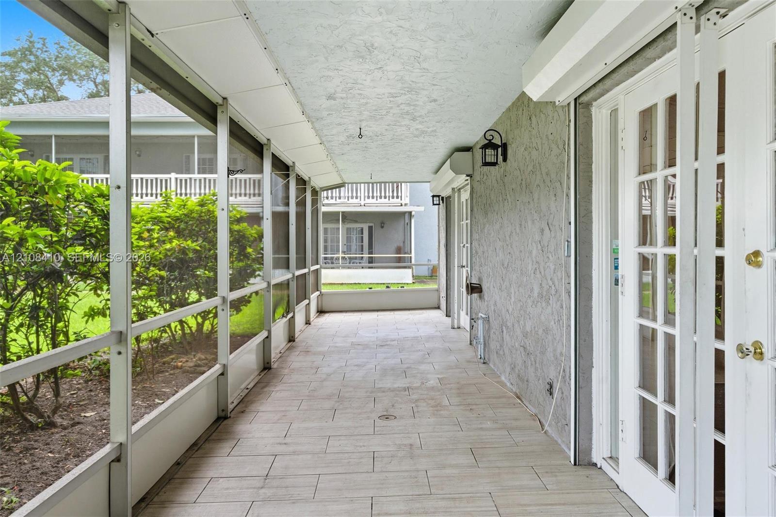 Screened-in lanai featuring large-format ceramic tile flooring, textured stucco exterior wall, and French door entry