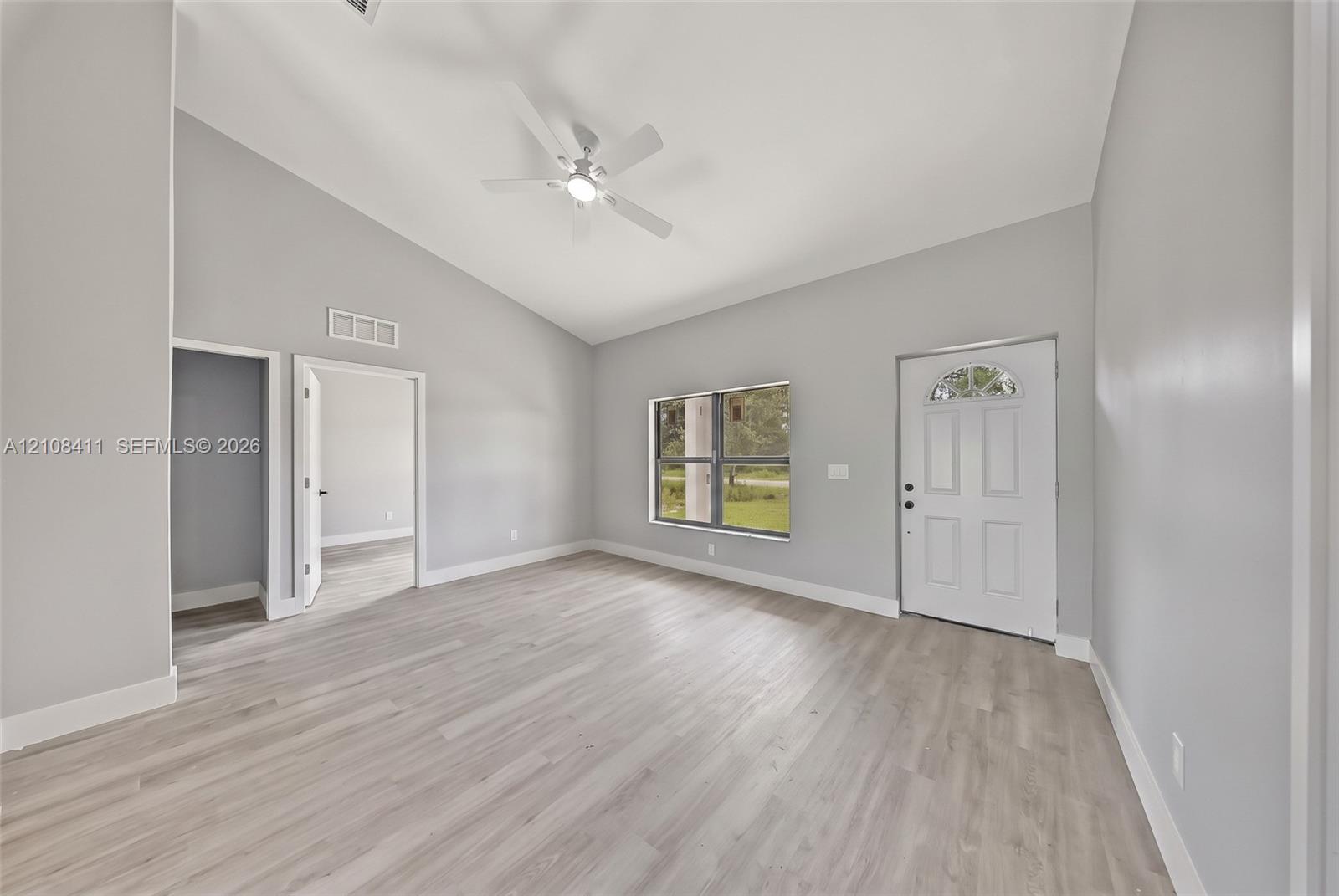 Interior space featuring vaulted ceilings, wood-finish flooring, a ceiling fan, and a six-panel exterior door with an arched glass insert Interior space featuring vaulted ceilings, wood-finish flooring, a ceiling fan, and a six-panel exterior door with an arched glass insert