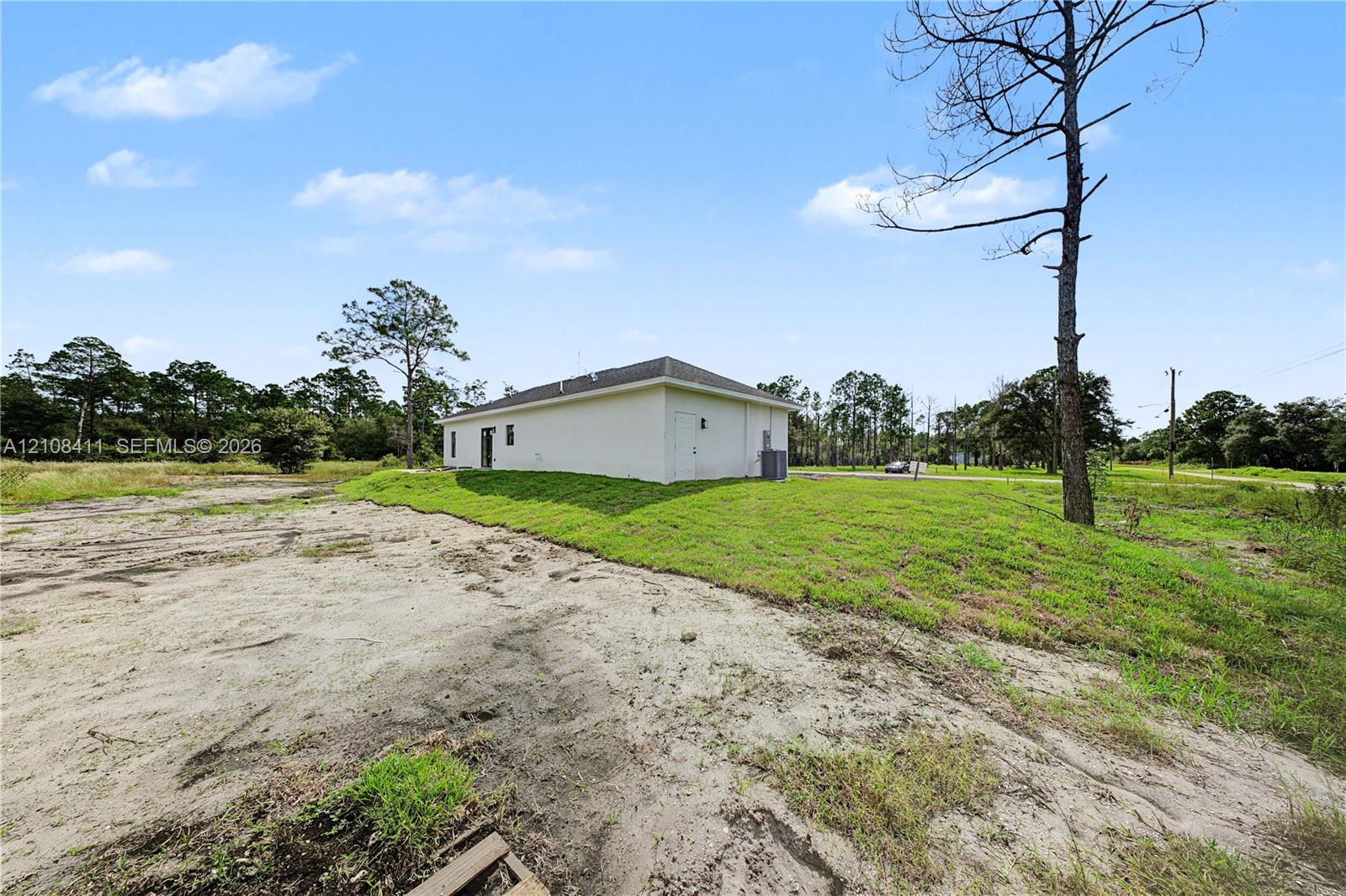 White exterior siding, hipped roofline, and expansive grounds featuring natural vegetation