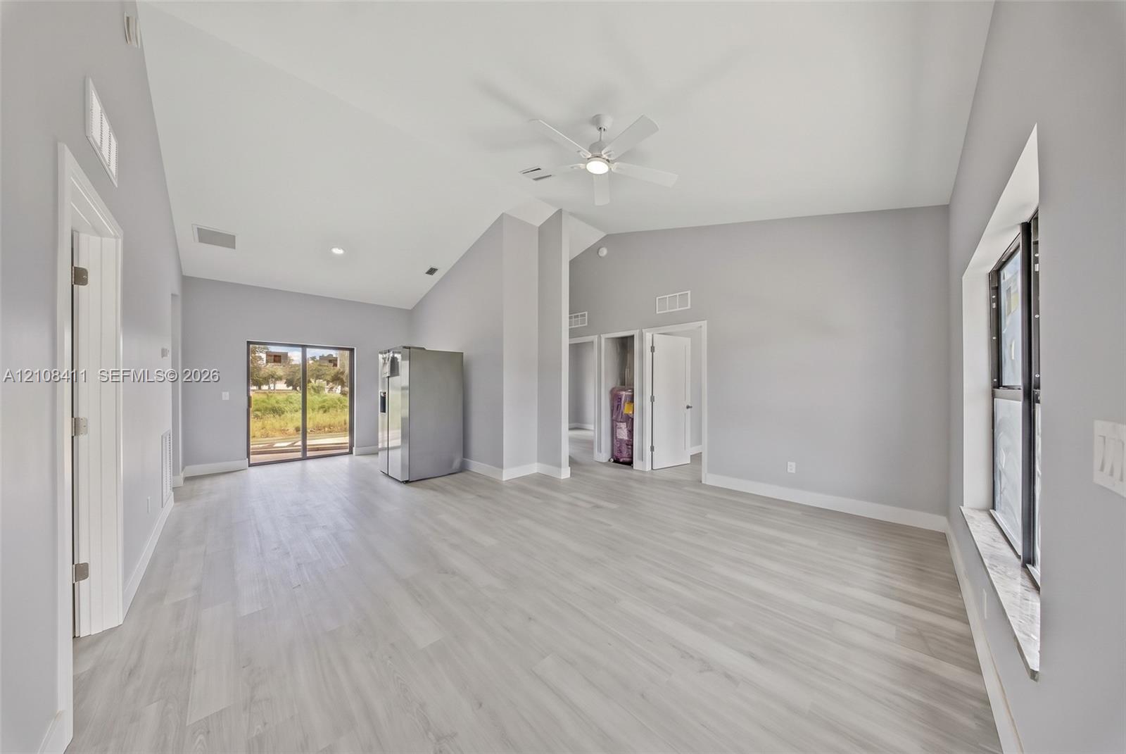 Open-concept interior featuring vaulted ceilings, wood-finish flooring, a ceiling fan, and sliding glass doors