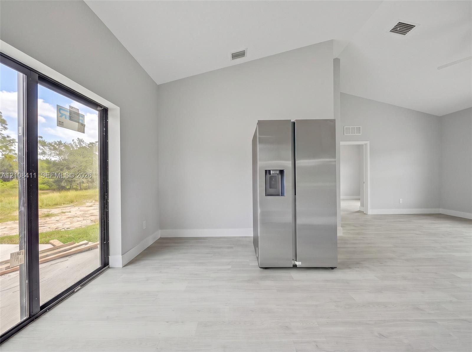 Vaulted ceilings, expansive glass sliding doors, wood-finish flooring, and a stainless steel side-by-side refrigerator
