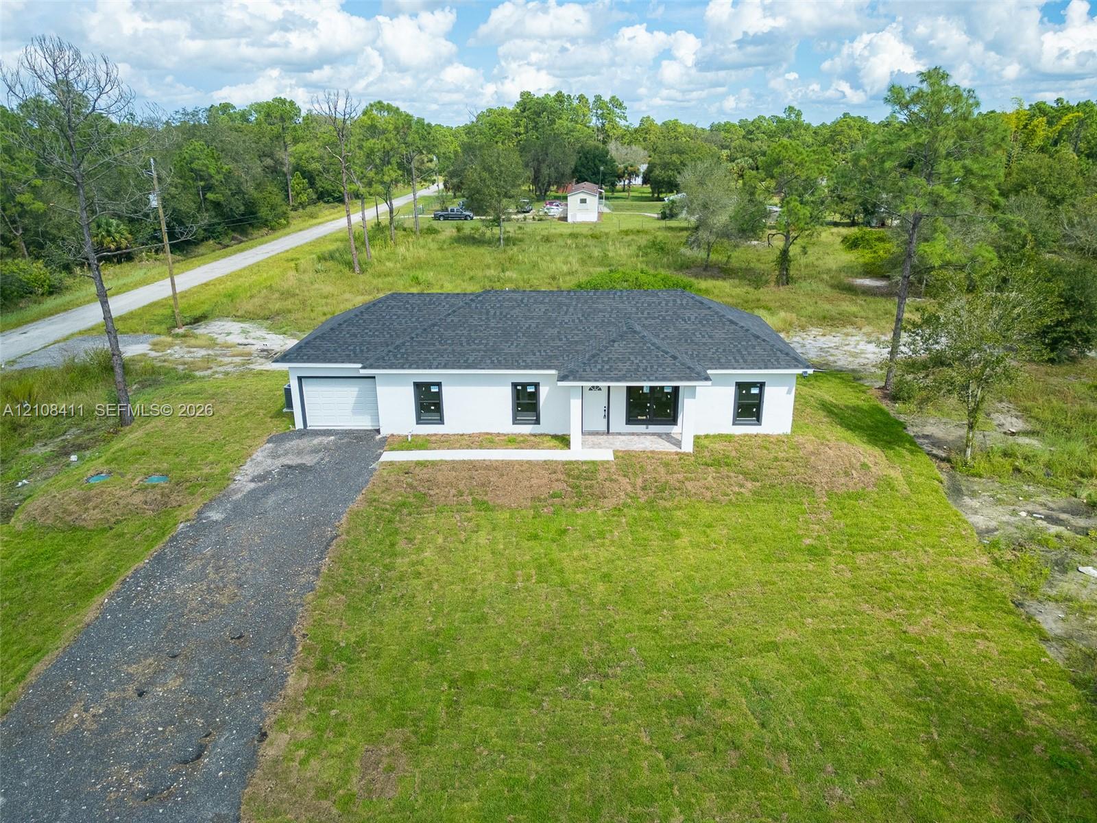 Single-story exterior featuring white stucco siding, a dark shingled roof, contrasting black window frames, and a gravel driveway Single-story exterior featuring white stucco siding, a dark shingled roof, contrasting black window frames, and a gravel driveway