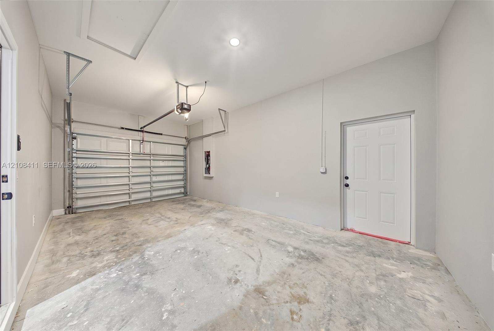 Finished garage featuring smooth-finish interior walls, a recessed ceiling light, an overhead garage door mechanism, and an exterior-access door