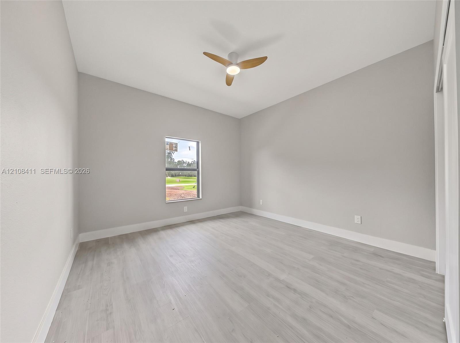 Neutral-toned interior space featuring wood-finish flooring, a contemporary three-blade ceiling fan with integrated lighting, and a single-pane window