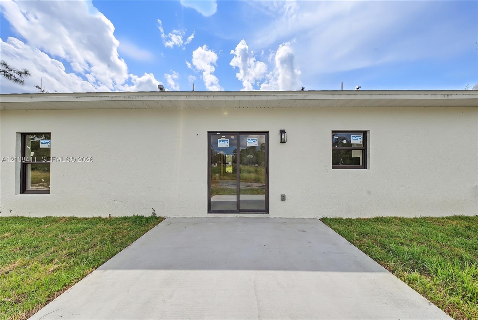 Stucco exterior finish, concrete patio, sliding glass door, and two single-pane windows with dark frames