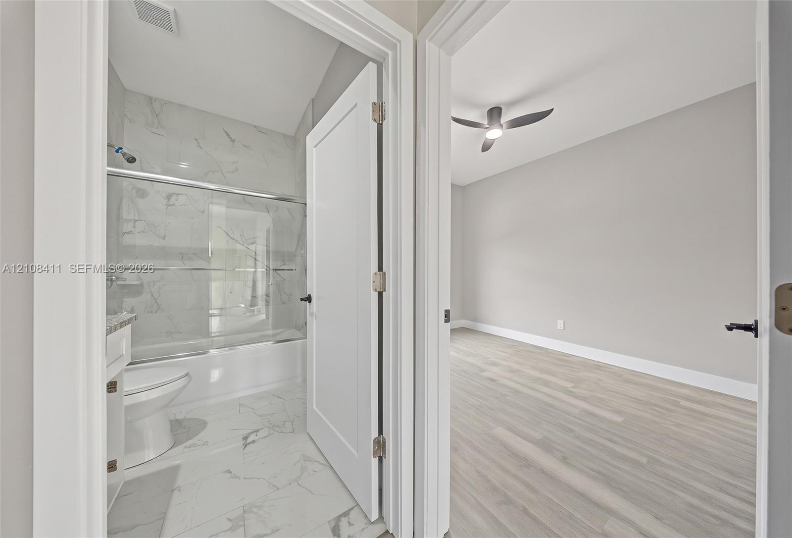Full bathroom with a tub-shower combination featuring tile surround, and an interior room with wood-finish flooring and a ceiling fan