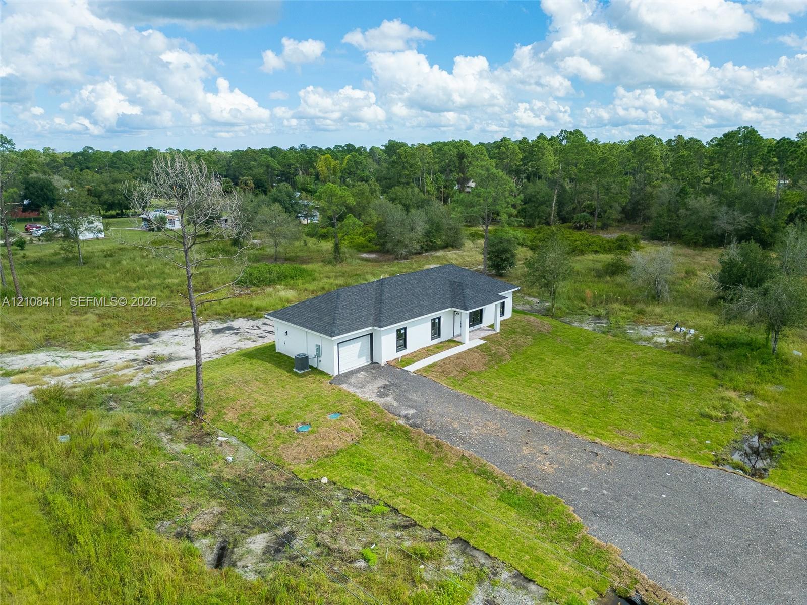 Single-story residence featuring a multi-hip roof, white exterior, attached garage, and a gravel driveway situated on a cleared lot Single-story residence featuring a multi-hip roof, white exterior, attached garage, and a gravel driveway situated on a cleared lot