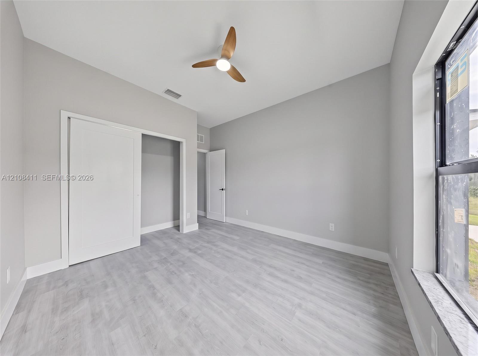 Neutral-toned interior featuring wood-finish flooring, a contemporary three-blade ceiling fan with integrated lighting, sliding closet doors, and a large window with a stone-finish sill