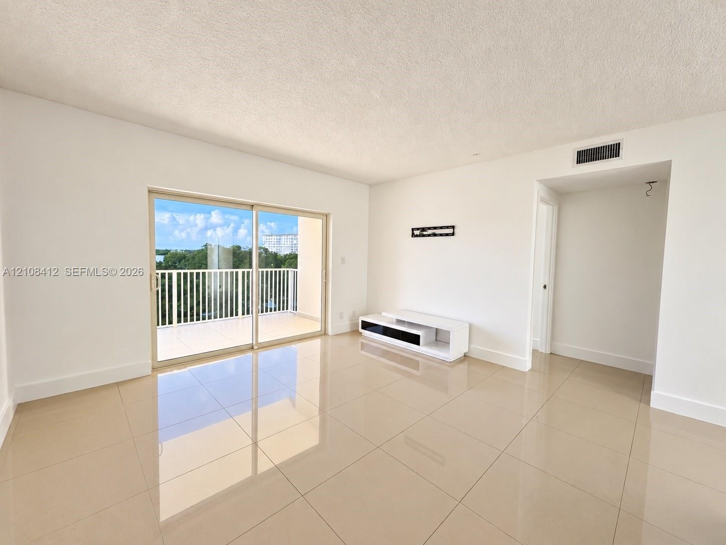 Interior space featuring large-format tile flooring, sliding glass doors providing outdoor access, and a balcony with white metal railings