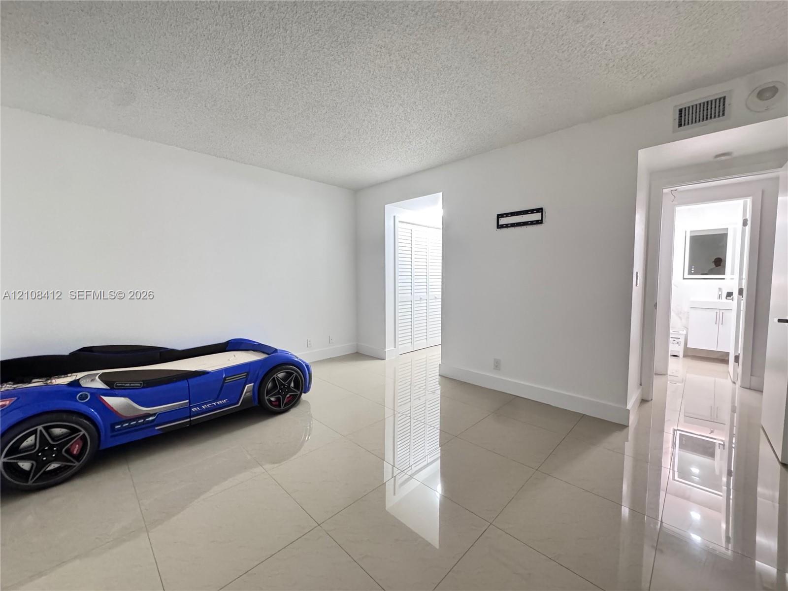 Neutral-toned large-format tile flooring throughout with white walls and louvered closet doors