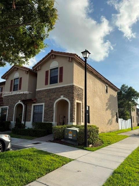 Two-story exterior featuring a stucco facade, stone veneer accents, arched entryway, and louvered shutters