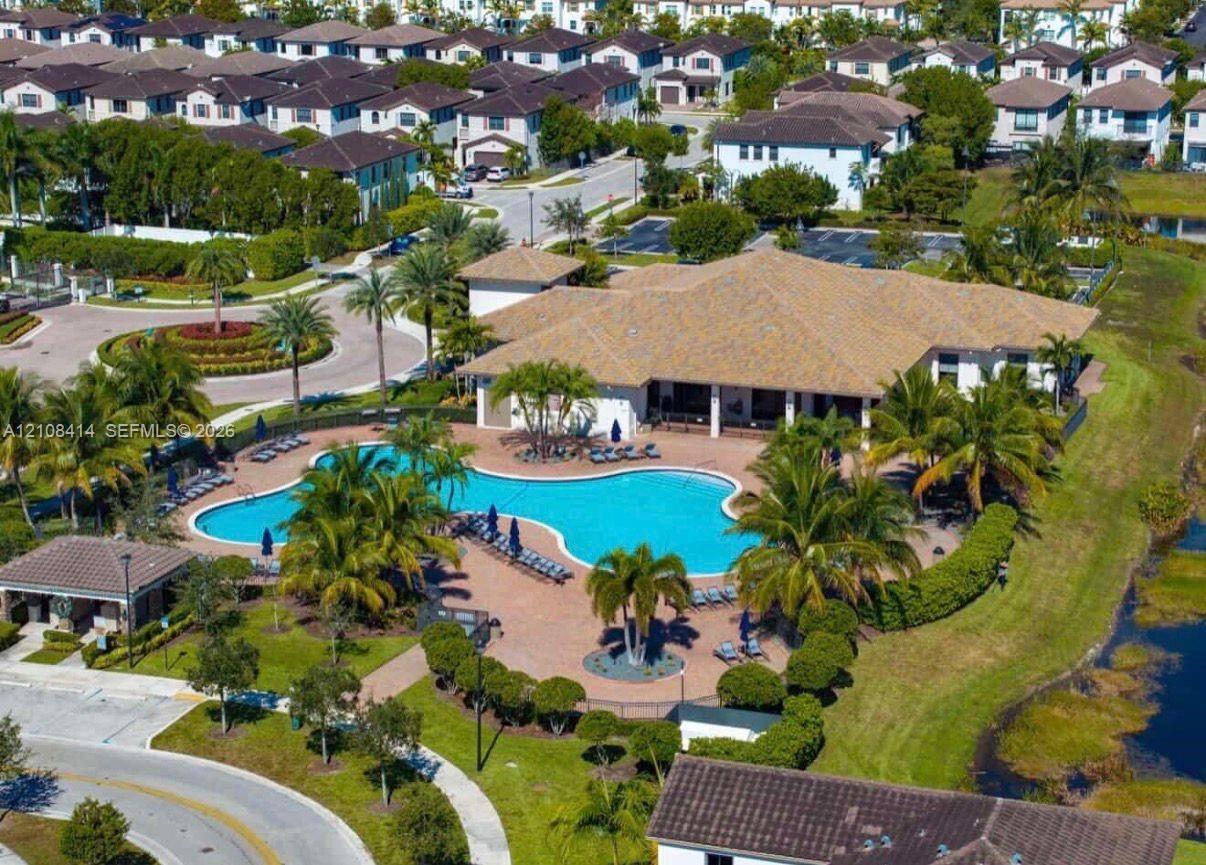 Aerial view of community clubhouse featuring a large swimming pool, paver deck, and landscaped grounds with mature palm trees