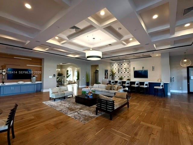 Coffered ceiling with integrated recessed lighting, wood-finish flooring, built-in cabinetry with wall-mounted television, and a service bar featuring pendant lighting