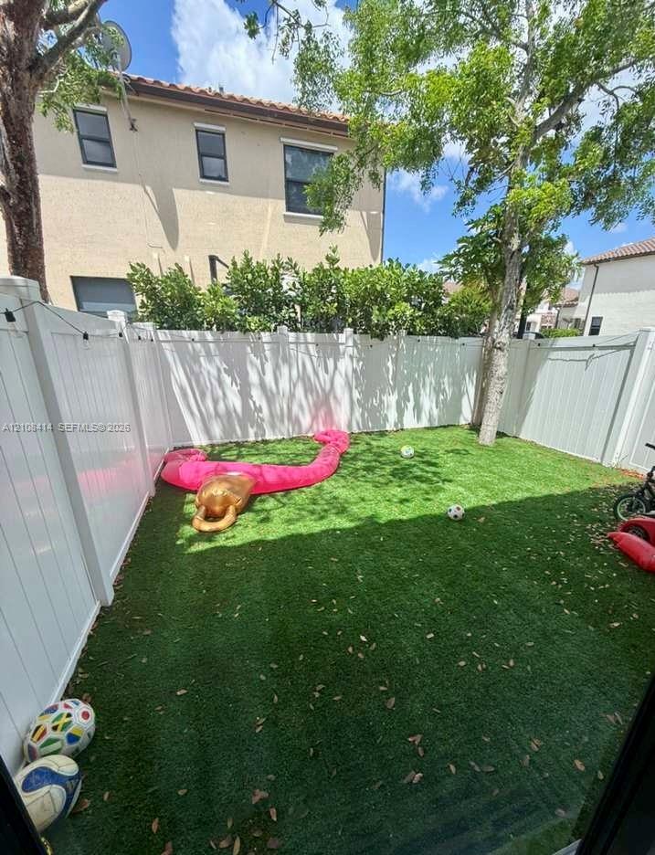 Enclosed backyard featuring synthetic turf and a full-height white vinyl privacy fence