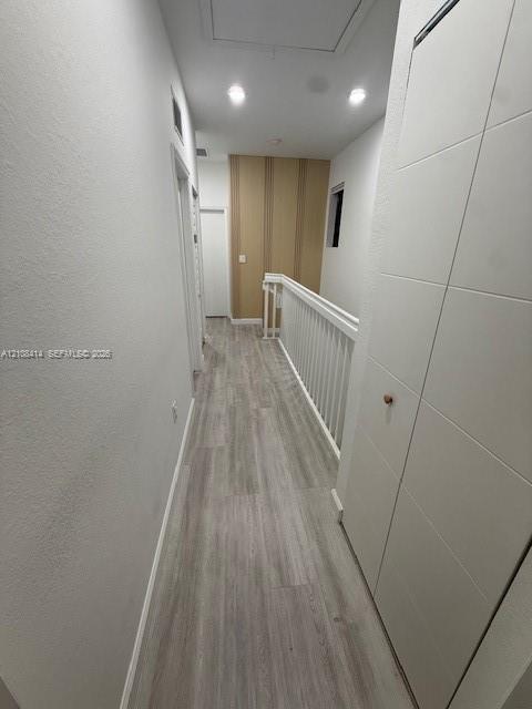 Hallway featuring wood-finish flooring, white paneled doors, recessed ceiling lighting, and a white baluster railing