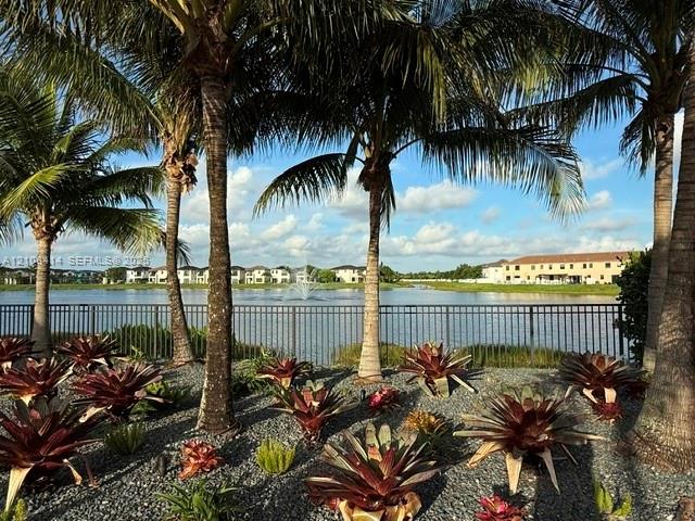 Waterfront landscaping featuring a gravel garden bed, ornamental tropical plants, mature palm trees, and a metal perimeter fence