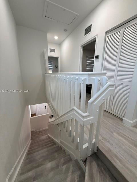 Staircase featuring a white wood balustrade and handrail, paired with light-toned wood-finish flooring and louvered bifold closet doors