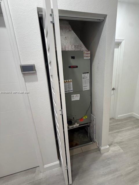 Utility closet housing a HVAC unit with louvered bi-fold door, wall-mounted digital thermostat, and wood-finish flooring