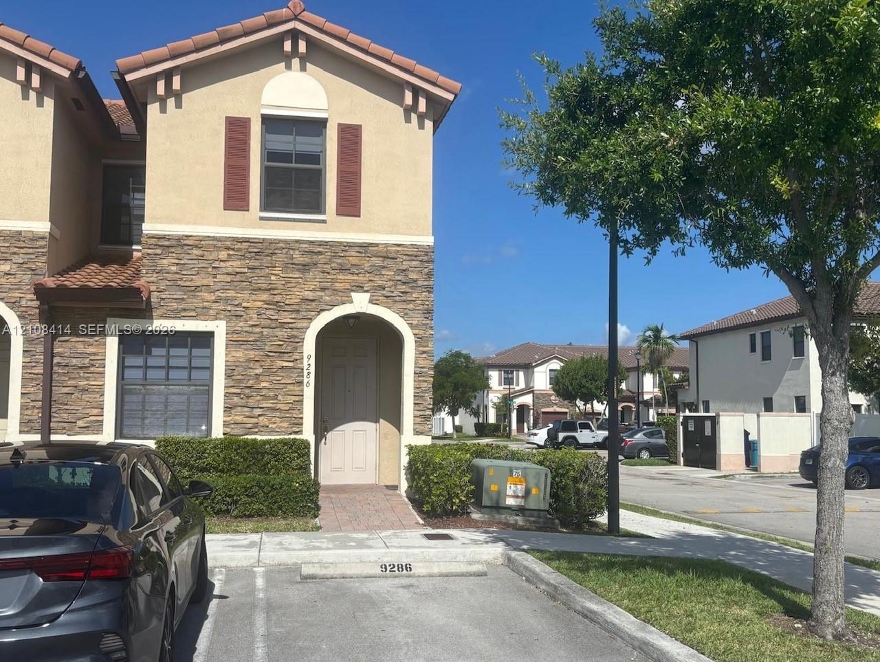 Multi-level exterior featuring tan stucco siding, stone veneer accents, arched entryway, and clay-tile roofing