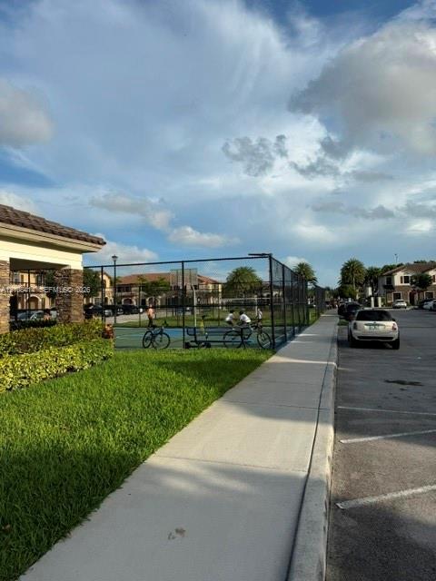 Fenced athletic court with blue surfacing, manicured lawn, and paved walkways